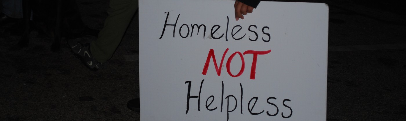 A person holding a handwritten sign that reads, "Homeless not helpless."