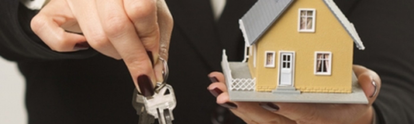Hands holding keys and a small model of a home