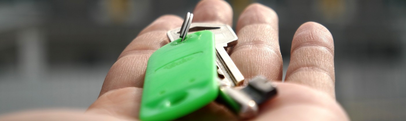 A hand holding out a set of keys on a green keychain