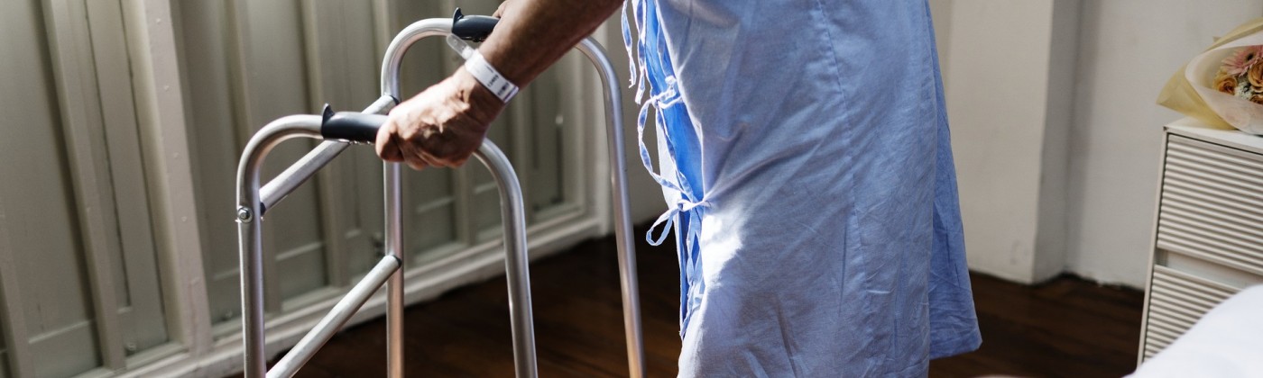 An elderly man in a hospital gown, leaning on a walker