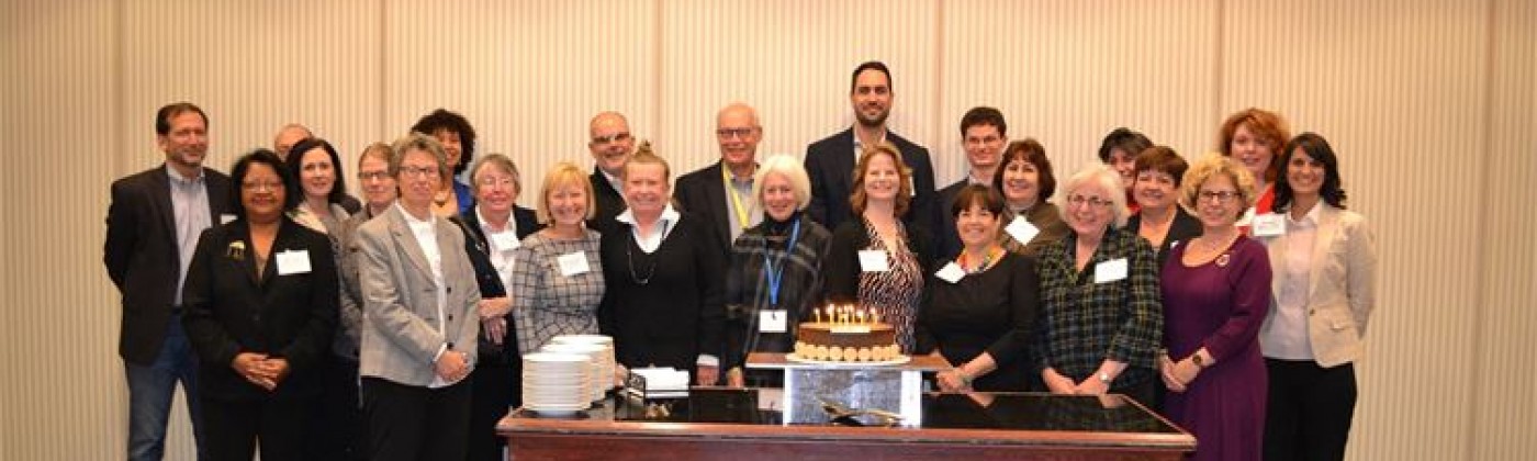 A line of people standing behind a table with a birthday cake