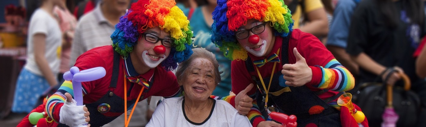 A smiling elderly woman in a wheelchair with two people dressed as clowns on either side