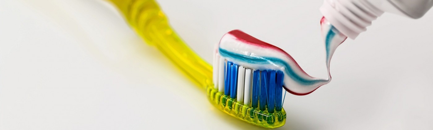 Striped toothpaste going on a yellow toothbrush