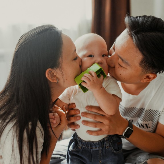 Two parents kissing their baby.