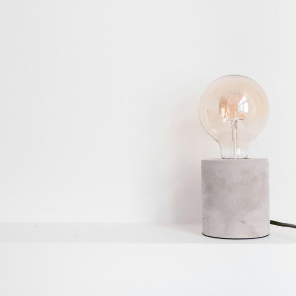 An image of a lamp with a clear lightbulb and a grey stone base.