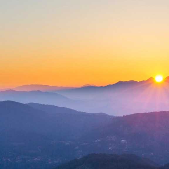 A picture of mountains with dark purple hues with bright orange sunset in the background