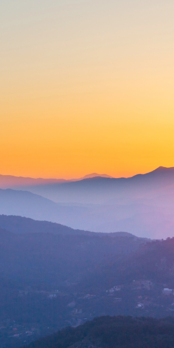 A picture of mountains with dark purple hues with bright orange sunset in the background