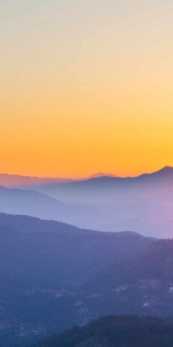 A picture of mountains with dark purple hues with bright orange sunset in the background
