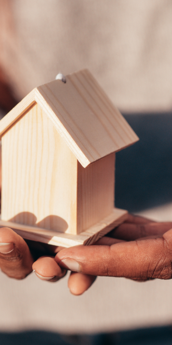 A picture of a couple with their hands holding a miniature wooden house together.