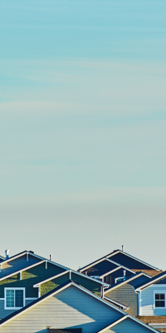 A sunset light blue sky with hues of orange as the backdrop amid a neighborhood - the tops of homes can be seen.