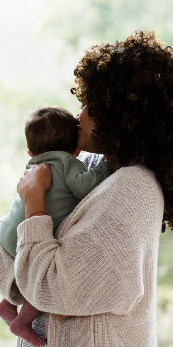 A picture of a mom holding her baby, as they look at out a window.