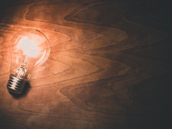 Migrated automatically. A lit light bulb, resting on its side on a wooden table.