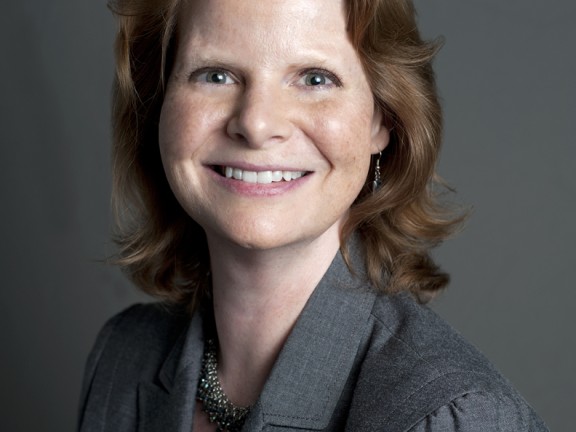 A smiling woman in a gray suit against a gray background