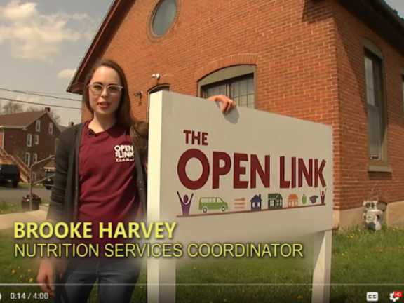 A young woman stands by a sign in front of a brick building.