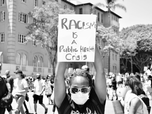 girl holding sign stating 'racism is a public health crisis'