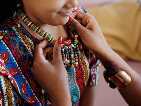 woman putting beaded necklace around child's neck during kwanzaa celebration