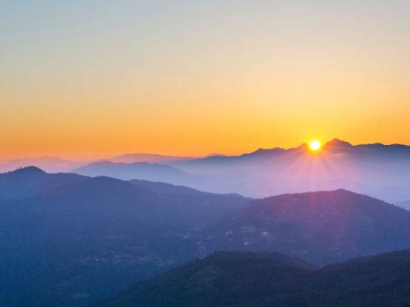 A picture of mountains with dark purple hues with bright orange sunset in the background