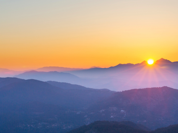 A picture of mountains with dark purple hues with bright orange sunset in the background