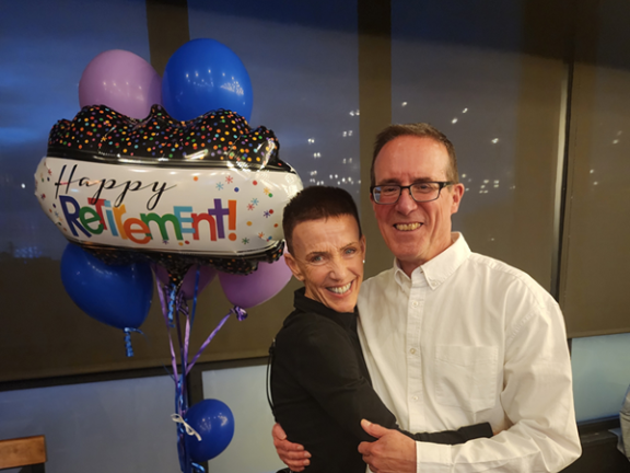 A couple smiling in front of a "Happy Retirement" balloon.