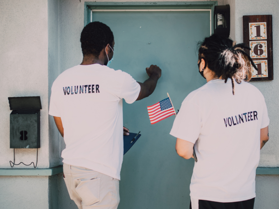 Two volunteers knocking on a blue door. 