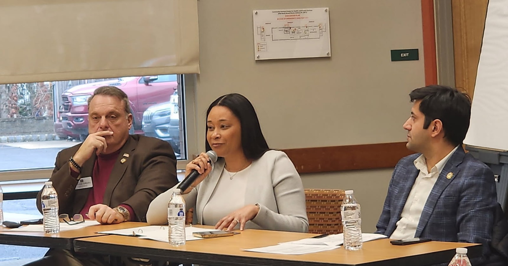 Three people sitting behind a brown table. 