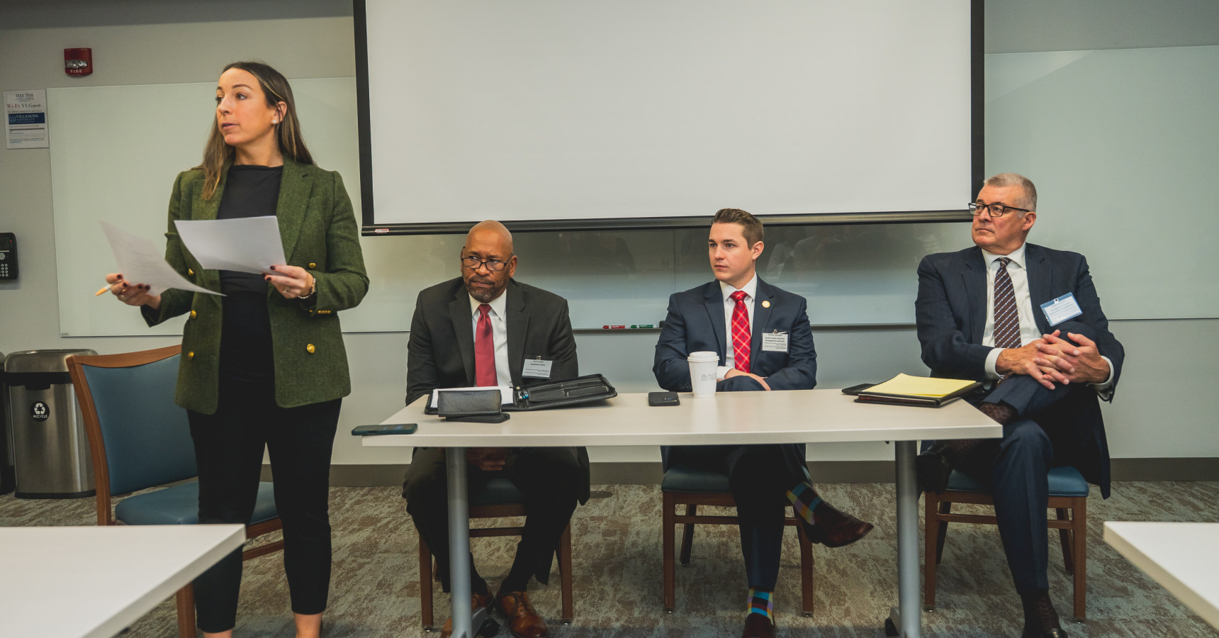 A panel of people preparing to speak, with the moderator standing up and talking to the crowd.