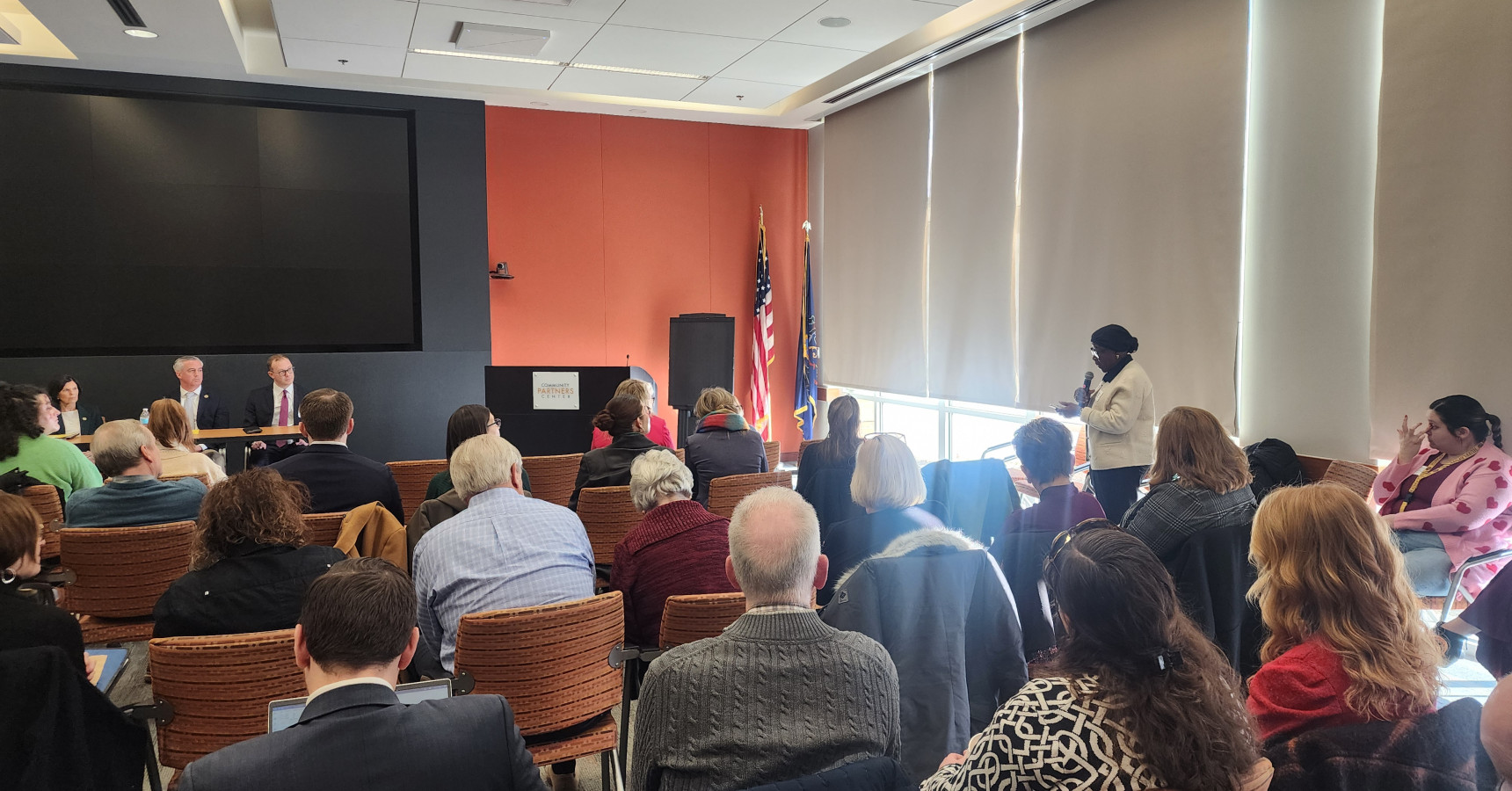 A lady in the audience holding a microphone, standing and asking a question to the three panelists sitting at a table.