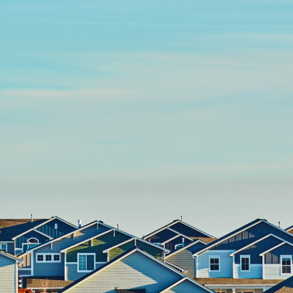 A sunset light blue sky with hues of orange as the backdrop amid a neighborhood - the tops of homes can be seen.