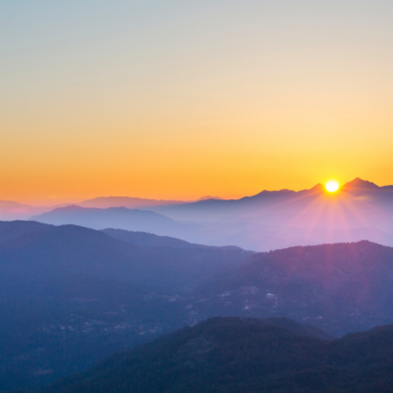 A picture of mountains with dark purple hues with bright orange sunset in the background