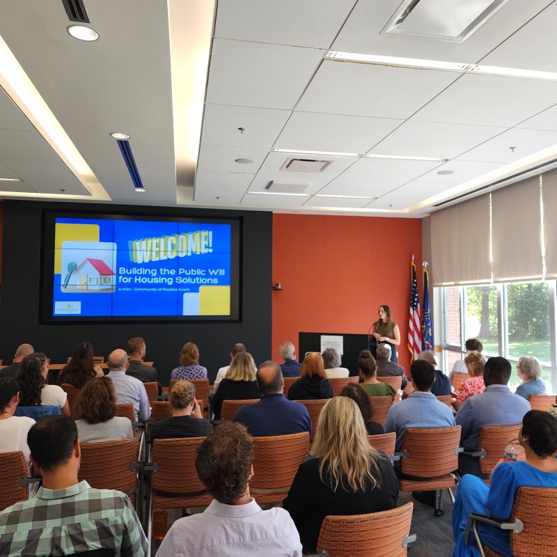 A picture of multiple rows of audience members listening to opening remarks from their event host.