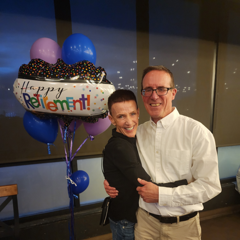 A couple smiling in front of a "Happy Retirement" balloon.