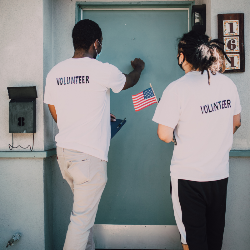 Two volunteers knocking on a blue door. 