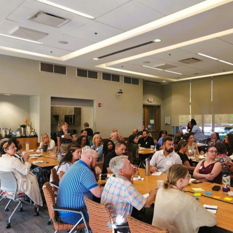 A group of people listening to a facilitator in a big conference room.