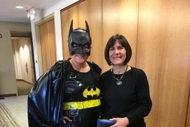 A woman receiving a present from someone dressed as a superhero.