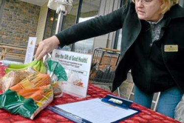 A woman stands behind a table that has a sign up sheet and back of carrots.