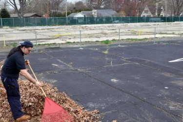 A man rakes leaves in a parking lot.