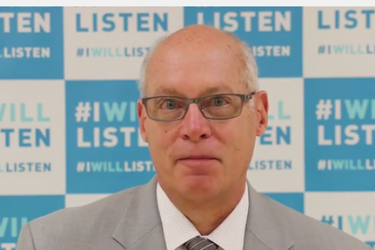 Head shot of a man in front of a background of repeating tiles that read, "I will listen."