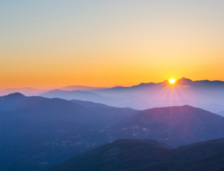 A picture of mountains with dark purple hues with bright orange sunset in the background