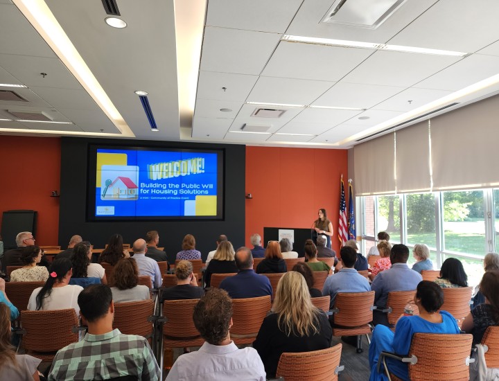 A picture of multiple rows of audience members listening to opening remarks from their event host.