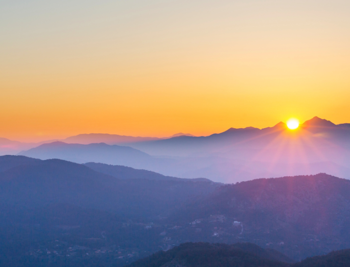 A picture of mountains with dark purple hues with bright orange sunset in the background