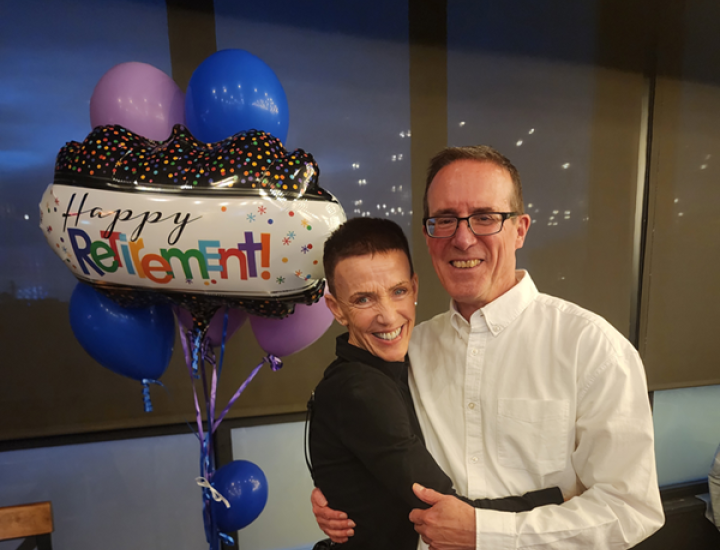 A couple smiling in front of a "Happy Retirement" balloon.
