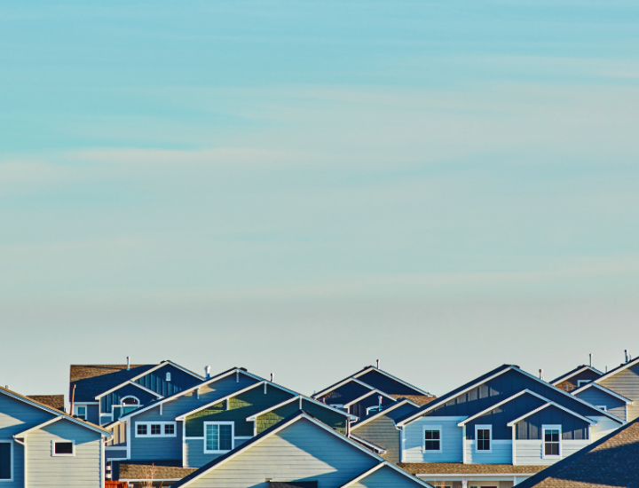A sunset light blue sky with hues of orange as the backdrop amid a neighborhood - the tops of homes can be seen.