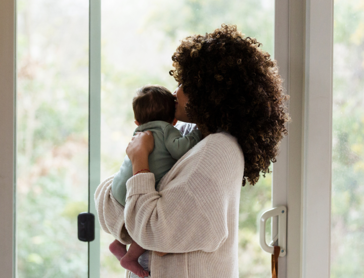 A picture of a mom holding her baby, as they look at out a window.