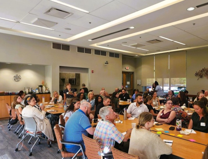 A group of people listening to a facilitator in a big conference room.